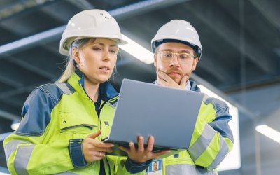 Low Angle Shot of Male and Female Industrial Engineers Work on a Manufacturing Plant, They Discuss Project while Using Laptop.In the Background Industrial Manufacturing Plant.